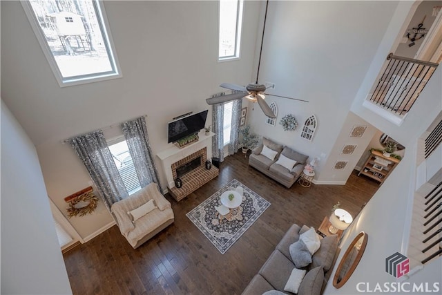 living area featuring a towering ceiling, plenty of natural light, a fireplace, and wood finished floors