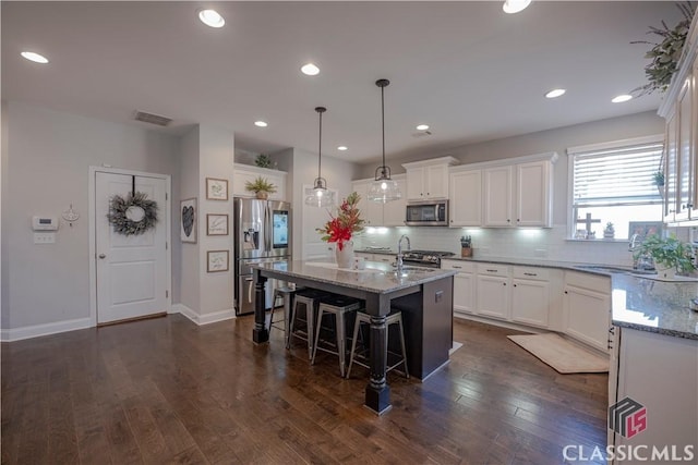 kitchen featuring light stone counters, stainless steel appliances, a breakfast bar, dark wood-style flooring, and visible vents