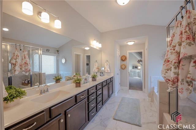 bathroom with marble finish floor, double vanity, vaulted ceiling, a sink, and a bath