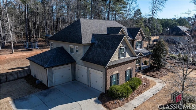 view of property exterior featuring a trampoline, roof with shingles, fence, a garage, and driveway