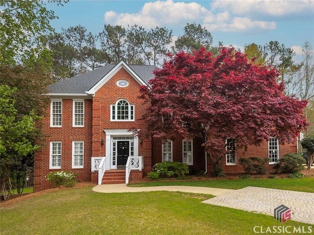 view of front of house featuring a shingled roof, a front lawn, and brick siding