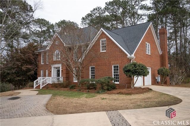 view of front facade featuring brick siding, a chimney, a shingled roof, concrete driveway, and an attached garage