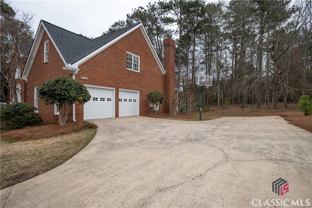 view of home's exterior featuring a garage, brick siding, a shingled roof, driveway, and a chimney