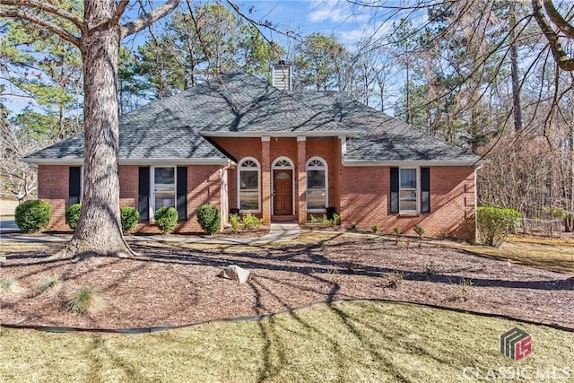 view of front of house featuring brick siding, roof with shingles, and a chimney