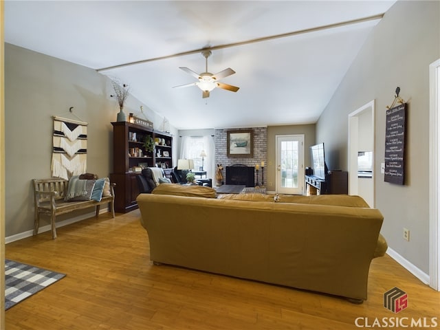 living room featuring ceiling fan, lofted ceiling, light wood-style flooring, baseboards, and a brick fireplace