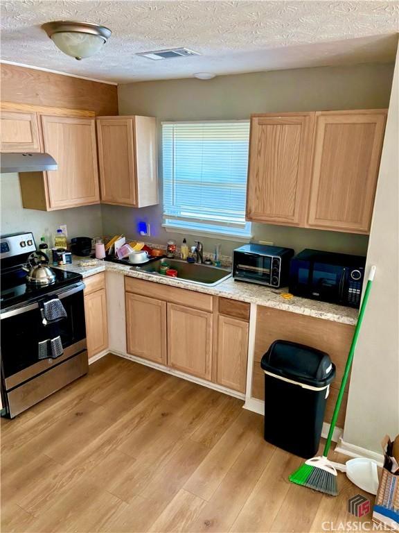 kitchen with black microwave, light brown cabinets, a sink, stainless steel electric stove, and light wood finished floors