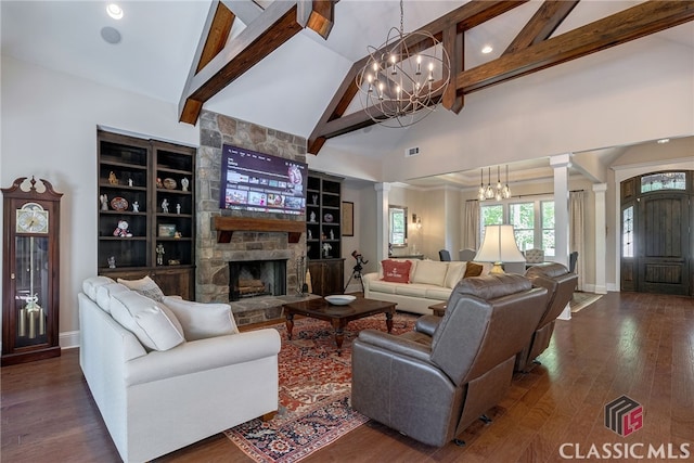 living area with decorative columns, dark wood-type flooring, a notable chandelier, and a stone fireplace