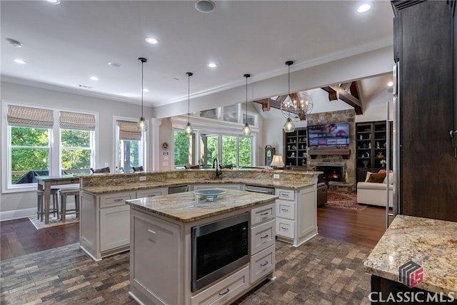 kitchen featuring a stone fireplace, a spacious island, open floor plan, built in microwave, and crown molding