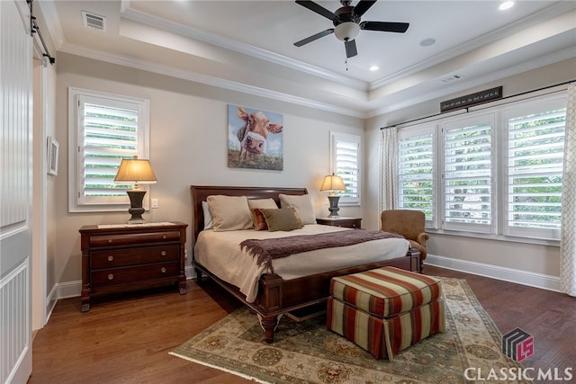 bedroom with ornamental molding, a tray ceiling, visible vents, and wood finished floors