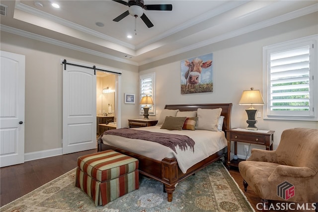 bedroom featuring a barn door, wood finished floors, baseboards, ornamental molding, and a raised ceiling