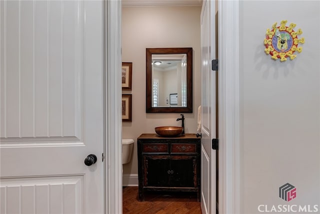 half bathroom with toilet, ornamental molding, wood finished floors, and vanity