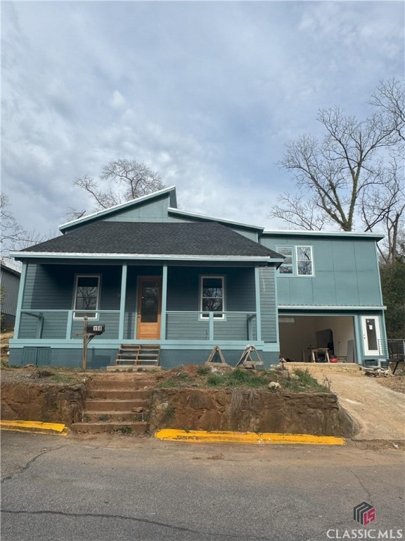 view of front facade featuring a porch, roof with shingles, and driveway