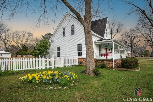 property exterior at dusk with a porch, a lawn, and a fenced front yard