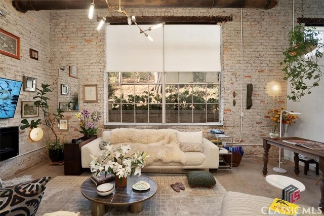 living area featuring brick wall, beam ceiling, concrete floors, and a towering ceiling