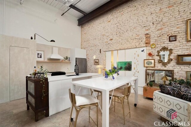 kitchen featuring brick wall, a high ceiling, a sink, and beamed ceiling