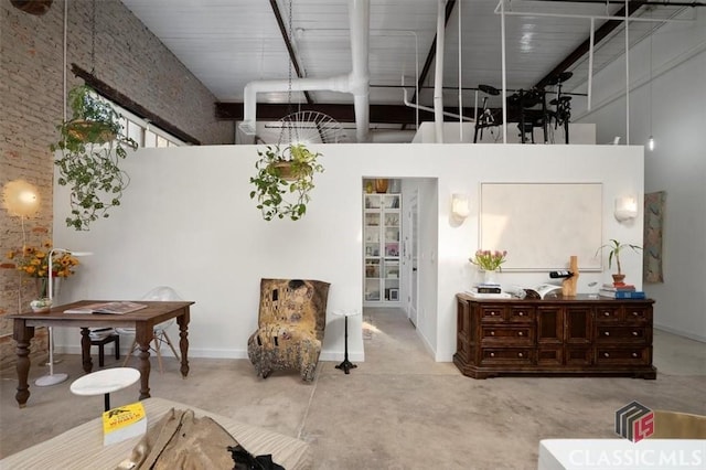 living area with a high ceiling, concrete floors, a glass covered fireplace, and beam ceiling