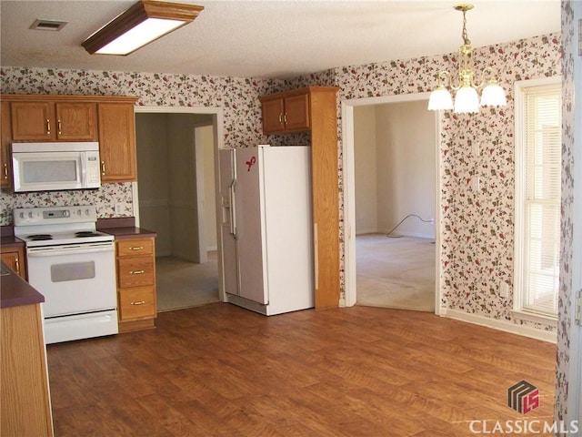 kitchen with white appliances, wallpapered walls, visible vents, dark countertops, and dark wood-type flooring