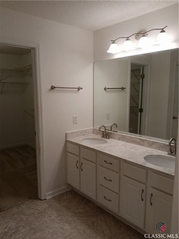 full bath with a walk in closet, a sink, and a textured ceiling