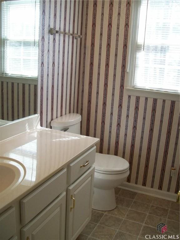 half bathroom featuring tile patterned flooring, toilet, vanity, baseboards, and wallpapered walls