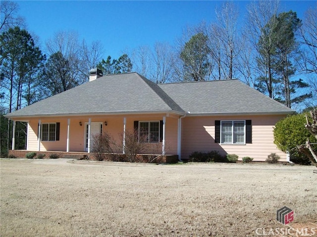 ranch-style house featuring roof with shingles, a porch, a chimney, and a front yard