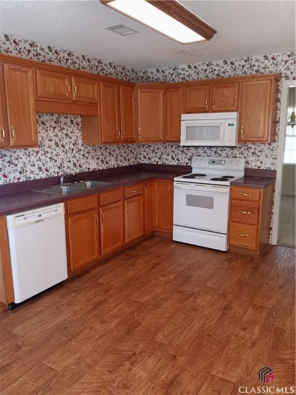 kitchen featuring white appliances, dark countertops, brown cabinets, light wood-style floors, and a sink