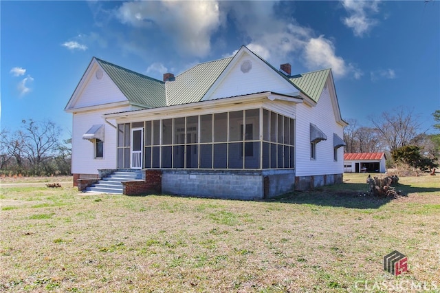 view of front of house with a sunroom, a chimney, metal roof, and a front yard