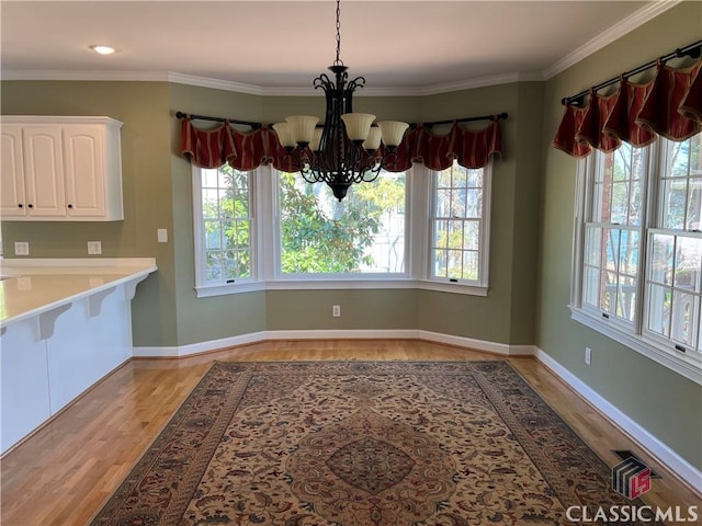 unfurnished dining area with a chandelier, plenty of natural light, crown molding, and light wood-style flooring