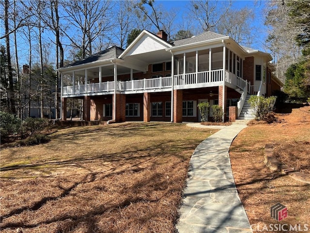 view of front of home with brick siding, a sunroom, stairway, a chimney, and a front yard