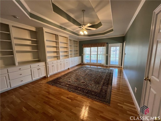 interior space with a raised ceiling, ceiling fan, baseboards, and wood finished floors