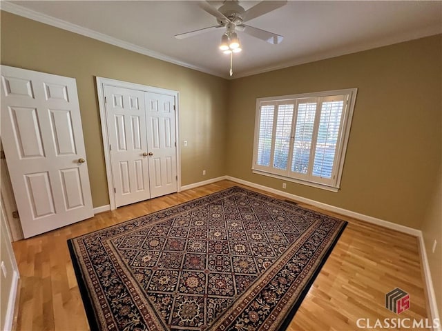 bedroom with crown molding, a closet, a ceiling fan, wood finished floors, and baseboards