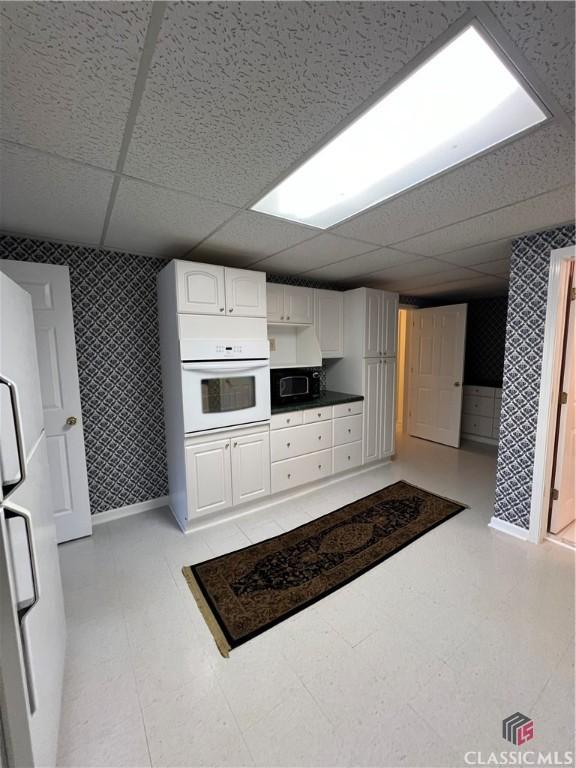 kitchen with white appliances, a drop ceiling, white cabinets, and wallpapered walls