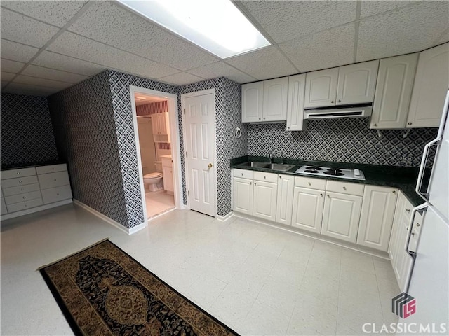 kitchen with a paneled ceiling, dark countertops, white cabinets, and under cabinet range hood