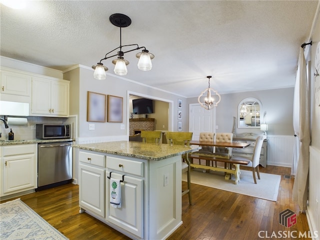 kitchen featuring dark wood-style floors, appliances with stainless steel finishes, wainscoting, a sink, and white cabinetry