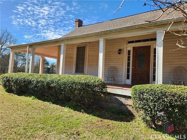 property entrance featuring a porch, a lawn, a chimney, and a shingled roof