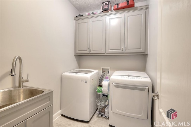 laundry room featuring a textured ceiling, a sink, independent washer and dryer, cabinet space, and light wood finished floors