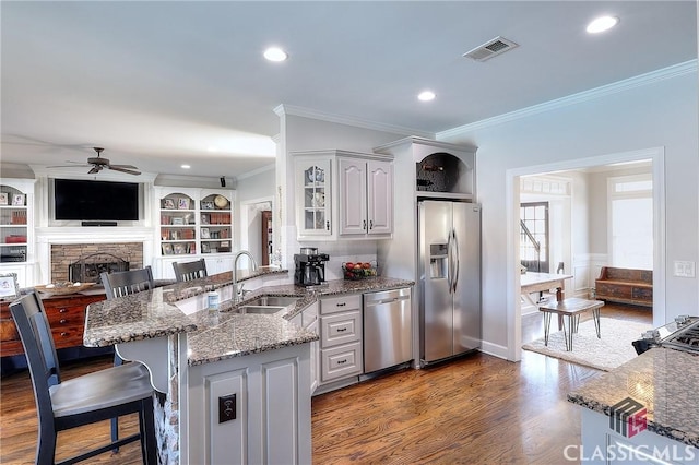 kitchen featuring a stone fireplace, a peninsula, wood finished floors, a sink, and appliances with stainless steel finishes