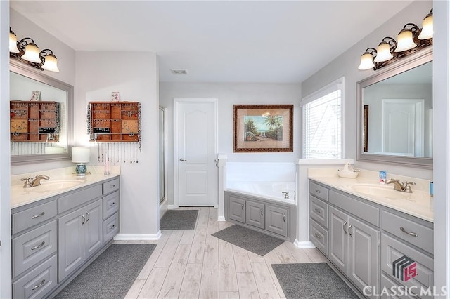 bathroom with two vanities, a sink, a bath, and wood finished floors