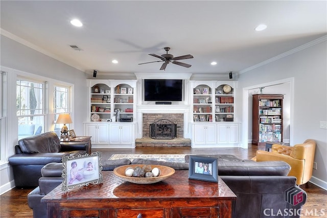 living room with visible vents, ornamental molding, a stone fireplace, wood finished floors, and baseboards