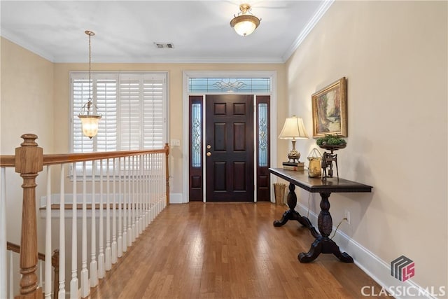 entryway with baseboards, crown molding, wood finished floors, and visible vents
