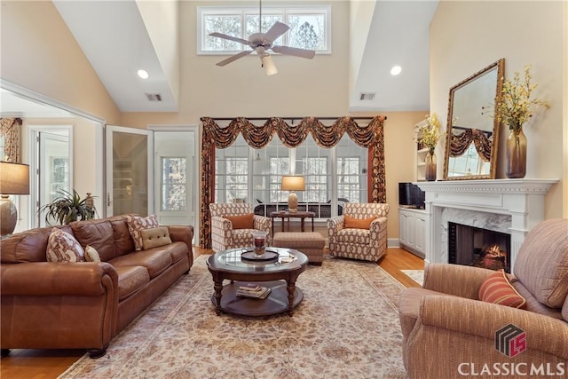 living room with ceiling fan, light wood-style floors, a premium fireplace, high vaulted ceiling, and visible vents