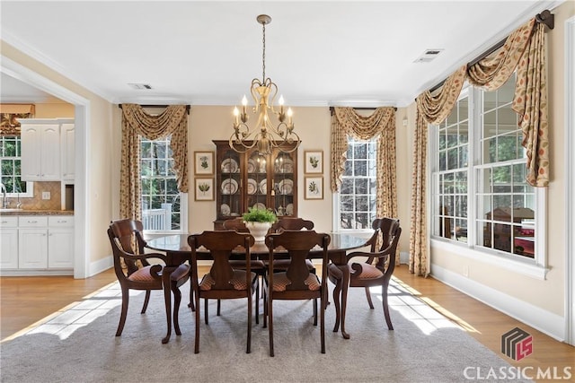 dining space with visible vents, ornamental molding, a notable chandelier, and light wood-type flooring