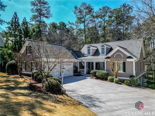 new england style home with a porch, an attached garage, and driveway