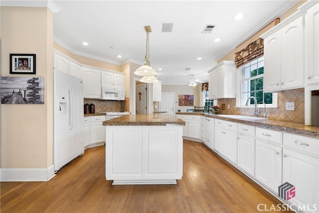 kitchen with a sink, a kitchen island, white appliances, and ornamental molding