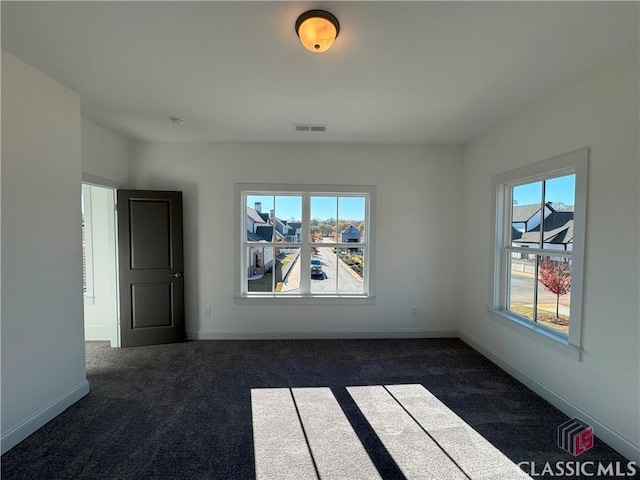 unfurnished room with plenty of natural light, visible vents, dark carpet, and baseboards