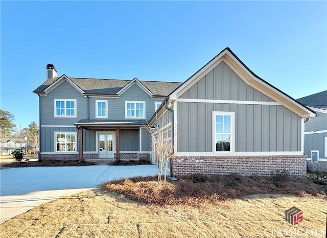 view of front of property featuring a chimney, french doors, board and batten siding, and brick siding