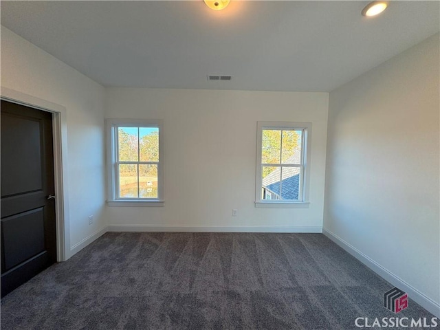 empty room with a healthy amount of sunlight, dark carpet, visible vents, and baseboards