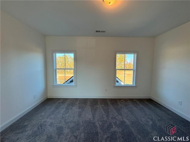 spare room featuring baseboards, dark colored carpet, visible vents, and a healthy amount of sunlight