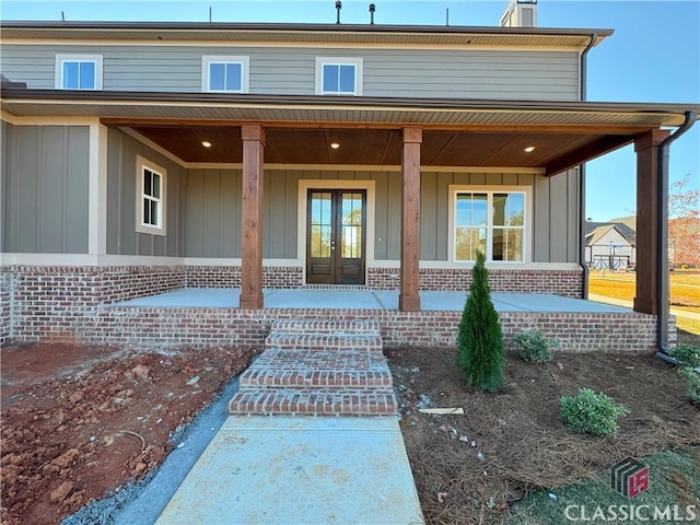 property entrance featuring brick siding, a porch, board and batten siding, and french doors