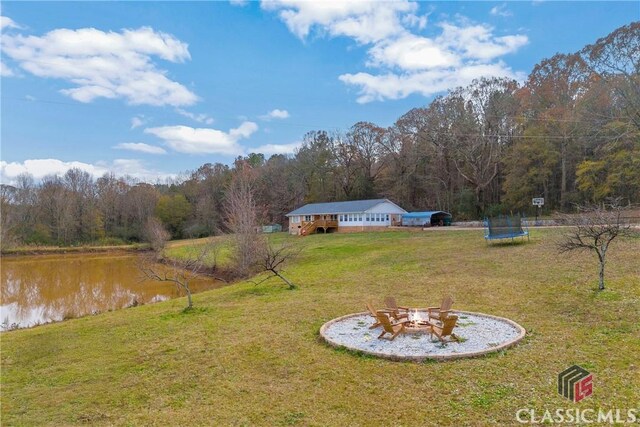 view of yard featuring a water view, a forest view, a trampoline, and a fire pit