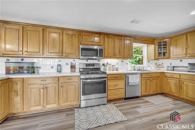 kitchen with stainless steel appliances, glass insert cabinets, light countertops, and visible vents